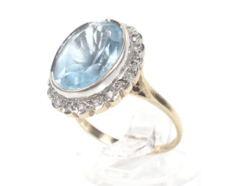 A vintage 9ct gold, blue topaz and diamond oval cluster ring. The oval mixed-cut pale blue topaz rub-over set within a tiny e