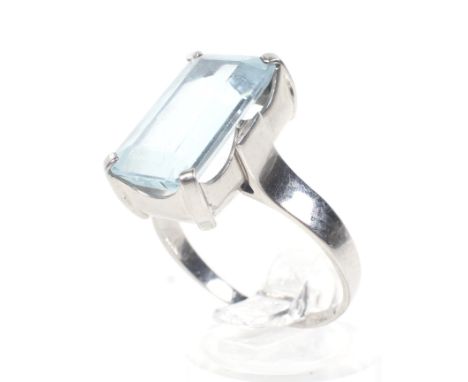 An aquamarine single stone ring. The pale blue rectangular step cut stone approx. 7.35cts, claw set between plain shoulders o