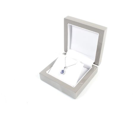 A modern platinum, tanzanite and diamond oval cluster pendant and chain. The pendant centred with an oval mixed-cut tanzanite