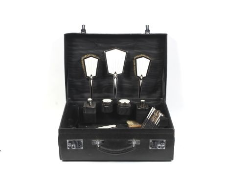 An Art Deco silver and enamel mounted travelling dressing table set, in a leather case. Comprising an angular hand mirror, tw