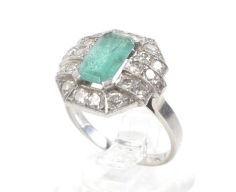 A French Art Deco emerald and diamond canted-rectangular cluster ring. Claw set aty the centred with an emerald-cut emerald w