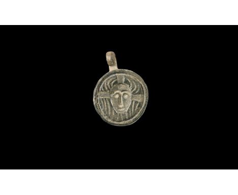 7th-10th century AD. A bronze discoid plaque with integral suspension loop above, mask of Christ facing on a textured field w