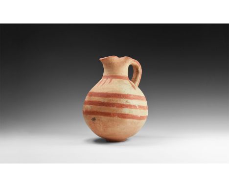 10th-6th century BC. A terracotta globular jug with basal ring, broad tubular neck with pinched sides and pouring lip, strap 