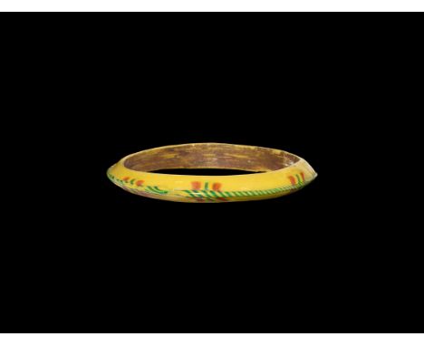 5th-8th century AD. An annular D-section yellow glass bangle with marvered twisted trails of yellow and green, pairs of red b