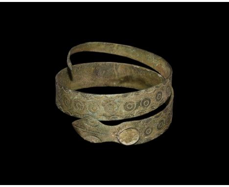 1st-2nd century AD. A bronze flat section coiled bracelet in the form of a snake; ring and dot motif to the entre of the body