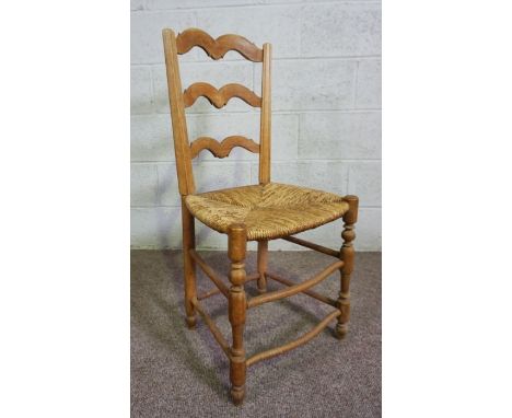A set of four ash framed ladder back dining chairs, 19th century, with rush seats, each with an elegant three stepped scroll 