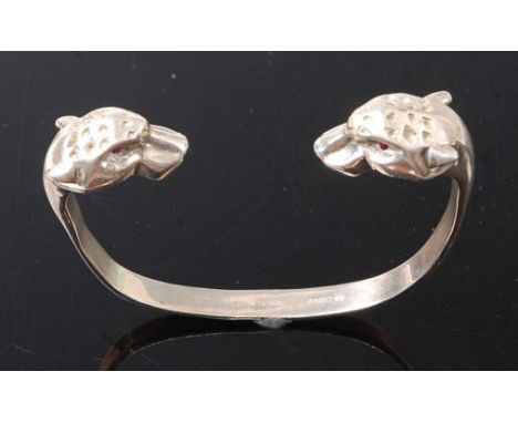 A sterling silver leopard head torque bangle, the two leopard heads each set with 1.2mm red stone eyes, bangle diameter appro