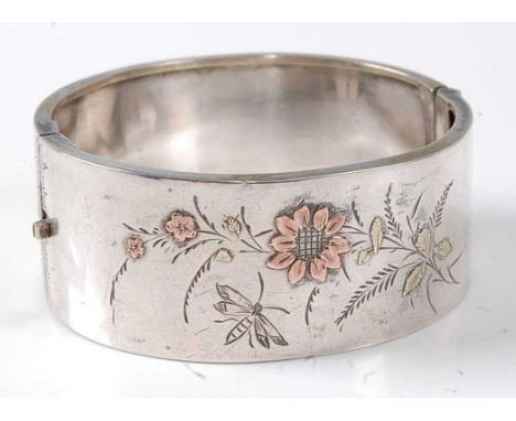 A Victorian white metal hinged bangle, having engraved leaf, flower and insect decoration, the flowers with two-colour yellow