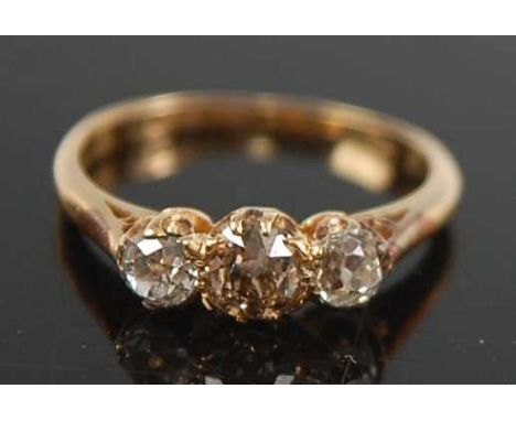 A yellow metal diamond three-stone ring, featuring a centre fancy light brown old cushion cut diamond with a cushion cut diam