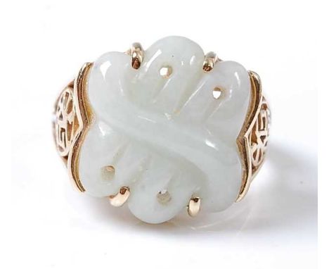 A 14ct yellow gold jadeite dress ring, featuring an abstract carved butterfly in pale jadeite, with trifurcated shoulders eac