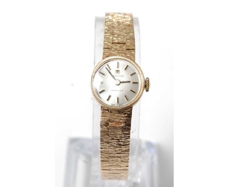 A lady's 9ct yellow gold Tissot manual wind wristwatch, having a round silver baton dial and an integral bark finish bracelet