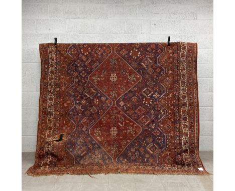 A 19th century Persian Kamseh carpet having three central diamond lozenge medallions in iron red over an abrash ground surrou