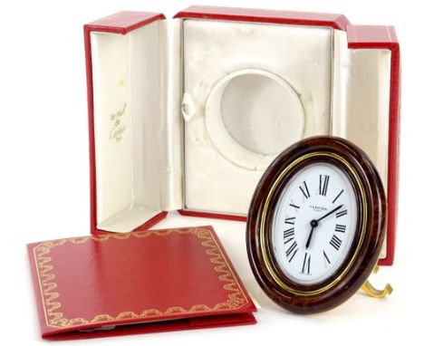 A Must De Cartier gilt metal travelling clock, with a simulated tortoiseshell enamel moulded front, the oval dial with Roman 