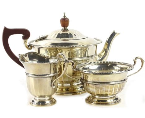 A George V silver three piece tea set, with a part faceted body, gadrooned border, the teapot with composition handle and kno