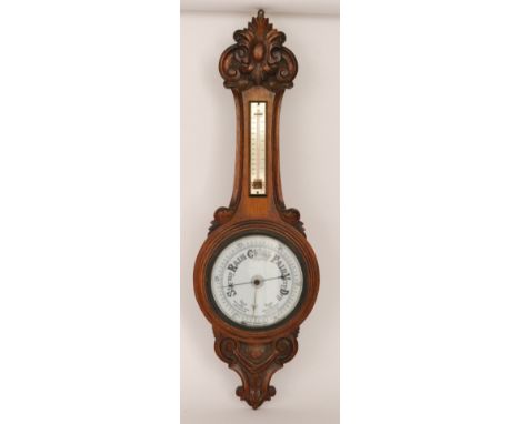 An early 20th Century carved oak aneroid wheel barometer with white enamelled dial and thermometer below carved scroll pedime
