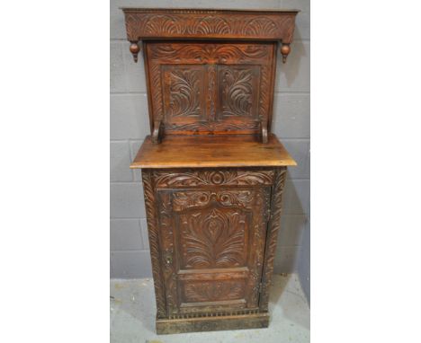 An oak livery or court style cupboard of small proportions, the canopy with carved frieze panel above a single door panel and