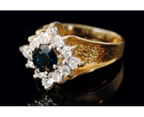 An 18ct sapphire and diamond cluster ring, central circular cut sapphire within a twelve brilliant cut diamond surround, all 