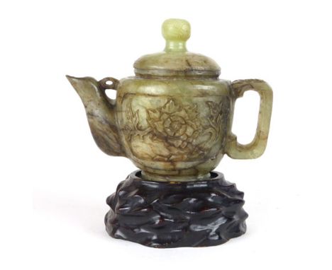 A Chinese jade type tea pot and cover, carved with scrolling floral decoration on a hardwood stand.  Height of tea pot 13 cm.