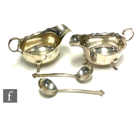 A pair of hallmarked silver sauce boats of plain form terminating in flying scroll handles and raised on three pad feet each 