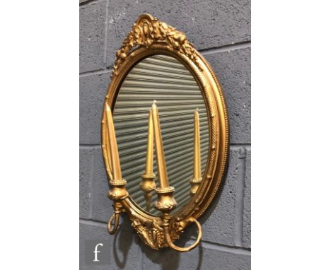A late 19th Century oval gilt girandole wall mirror, twin scroll branch arms below a pediment, 56cm x 37cm. 