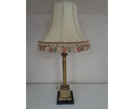 An antique brass Corinthian column table lamp on a black marble base 