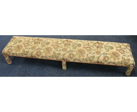 20th century fender footstool, upholstered in floral fabric, raised on square supports, 184cm x 39cm.