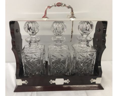 A modern mahogany triple Tantalus with 3 pressed glass decanters and 3 silver plate decanter labels. Labels are for Sherry, B