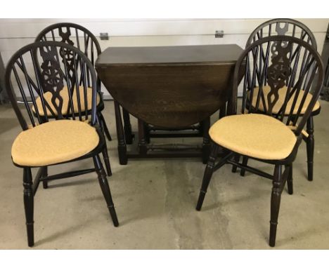 A vintage dark wood drop leaf, gate leg table with turned legs. Together with 4 dark wood wheel back kitchen chairs with gold