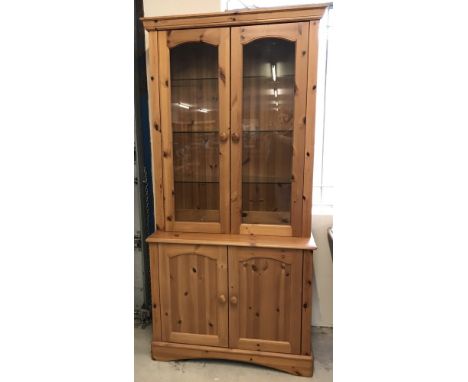 A modern honey pine glass fronted double dresser with interior lighting. 2 door cupboard with interior shelf to base with gla