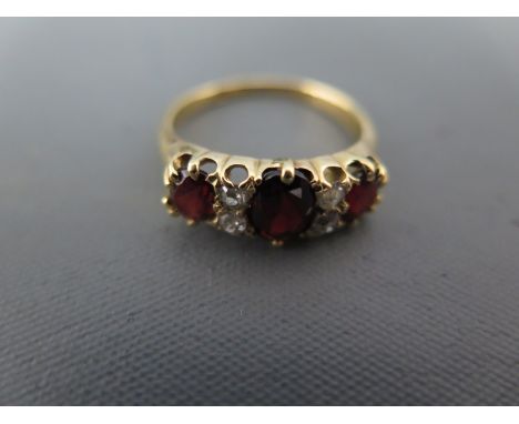 A garnet and diamond yellow gold ring, three oval cut garnets separated with four diamond - ring size N - approx weight 4 gra