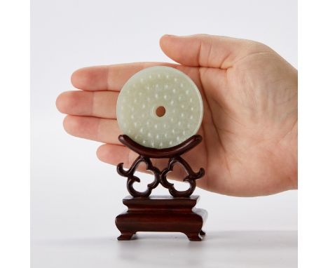Carved Chinese celadon jade bi. Carved on one side with repeating scrolls and along the other with dots. With a carved wooden
