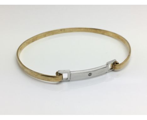 A 9ct yellow and white gold bangle, inset with a single diamond, total weight approximately 8 grams.