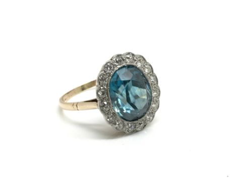 A yellow metal ring inset with a central large blue topaz surrounded by diamonds, ring size approximately S, total weight app