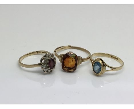 Three 9ct gold rings one set with a ruby and small chip stone diamonds, an amber Quartz and pale blue stone.