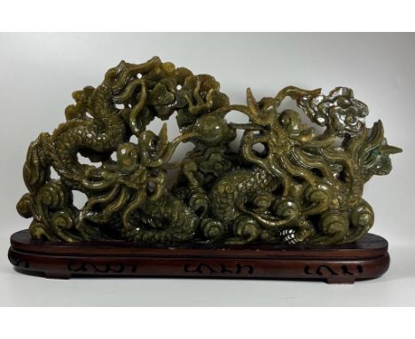 A LARGE CHINESE CARVED JADE TYPE GREEN HARDSTONE SCULPTURE DEPICTING TWO DRAGONS FIGHTING OVER THE FLAMING PEARL, ON WOODEN D