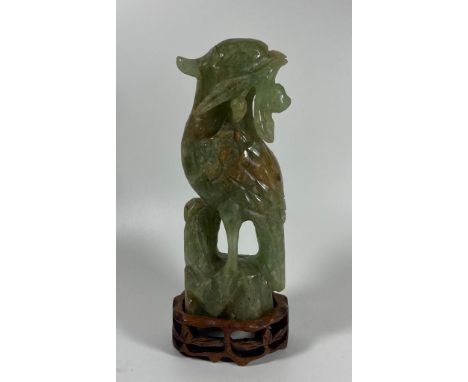 A CARVED JADE STYLE HARDSTONE MODEL OF A BIRD ON A CARVED WOODEN BASE, HEIGHT 20 CM 