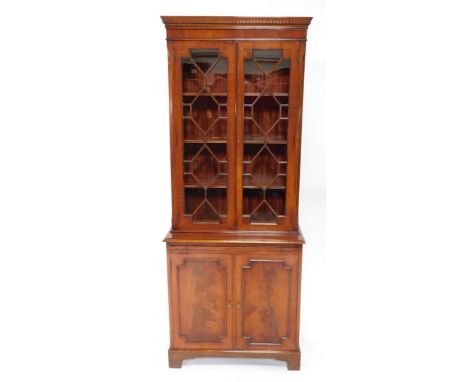 A Georgian style mahogany cupboard bookcase, the dentil moulded pediment over a pair of astragal glazed doors, enclosing thre