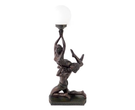 An Art Deco style bronzed figural table lamp, moulding as a kneeling man holding aloft a woman, in turn holding a frosted gla