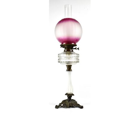 An Edwardian-style oil lamp, cranberry glass style opaque shade to clear reserve, to slender column support and metal ornate 