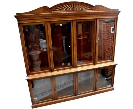 A large late Victorian oak bookcase with shell carved pediment above four glazed doors enclosing adjustable shelves, above a 