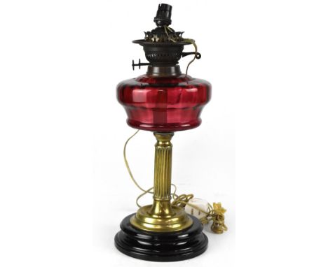 An Edwardian cranberry glass oil lamp on a reeded brass column and turned wooden base, converted to electricity, height 41cm.