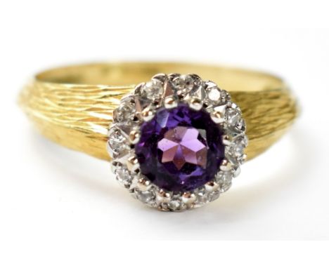 A vintage 18ct gold ring with central claw set amethyst stone in a halo of small white stones, with textured shoulders, size 