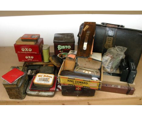 A box containing a collection of various tins and other items including cut throat razors, a trouser press, leather brief cas