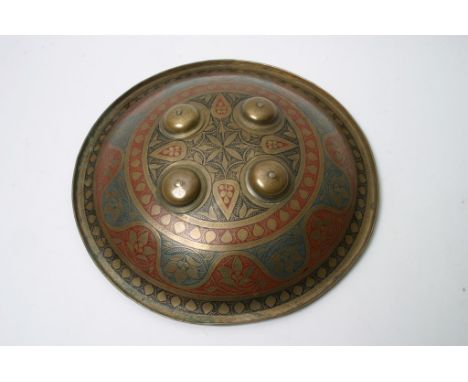A Middle Eastern brass shield of domed form engraved with blue, red and black enamel