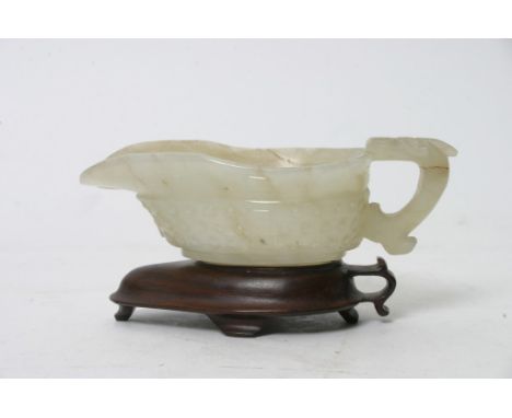 A well carved Chinese jade jug of archaic form on conforming wooden base. Length: 9.5cm approximately