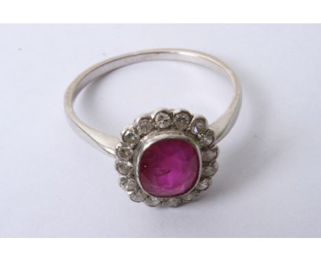 A ladies white gold ring set with a central oval cut ruby with diamond surround