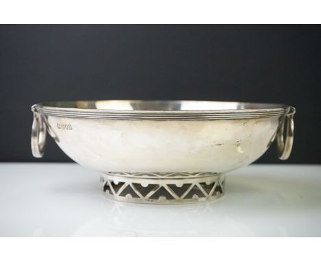 Large silver circular bowl of plain polished form, with two swing handles, raised on a pierced foot, London 1906, makers R&am