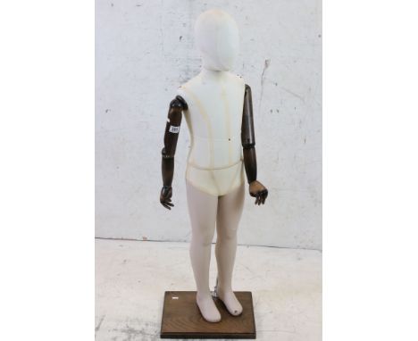 Child Shop Mannequin with cloth covered head and body, wooden articulated arms and hands, composite legs, mounted on a plinth