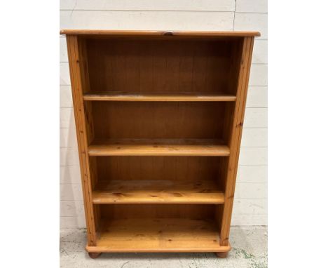 A pine three shelf bookcase on bun feet (H125cm W87cm D29cm)