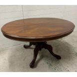 A mahogany oval tilt top centre table on turned central column with four acanthus scrolled down